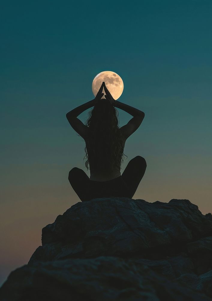 A woman silhouette sitting put the hand together above the head or doing yoga on the mountain in front of the moon astronomy…