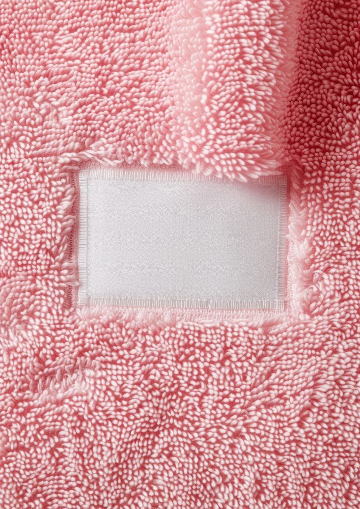 Empty white cotton long rectangle label vertical sewn on flatten pink towel backgrounds textured clothing.
