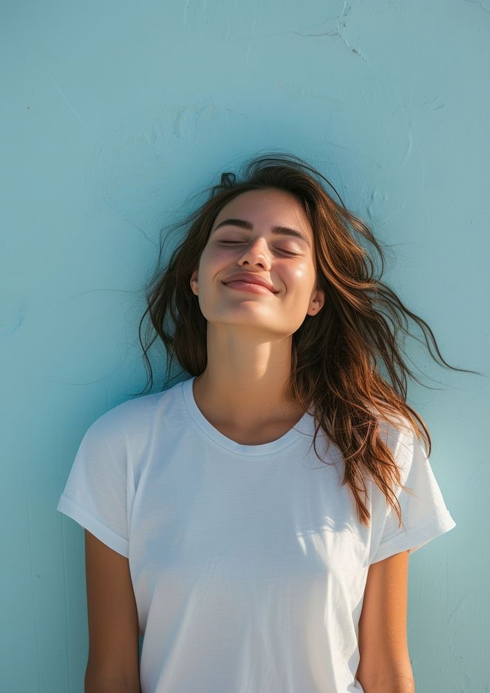 A happy woman wearing white t shirt smile blue wall.