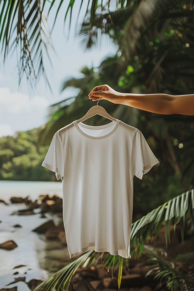 Hand holding hanger with white t shirt outdoors t-shirt sleeve.