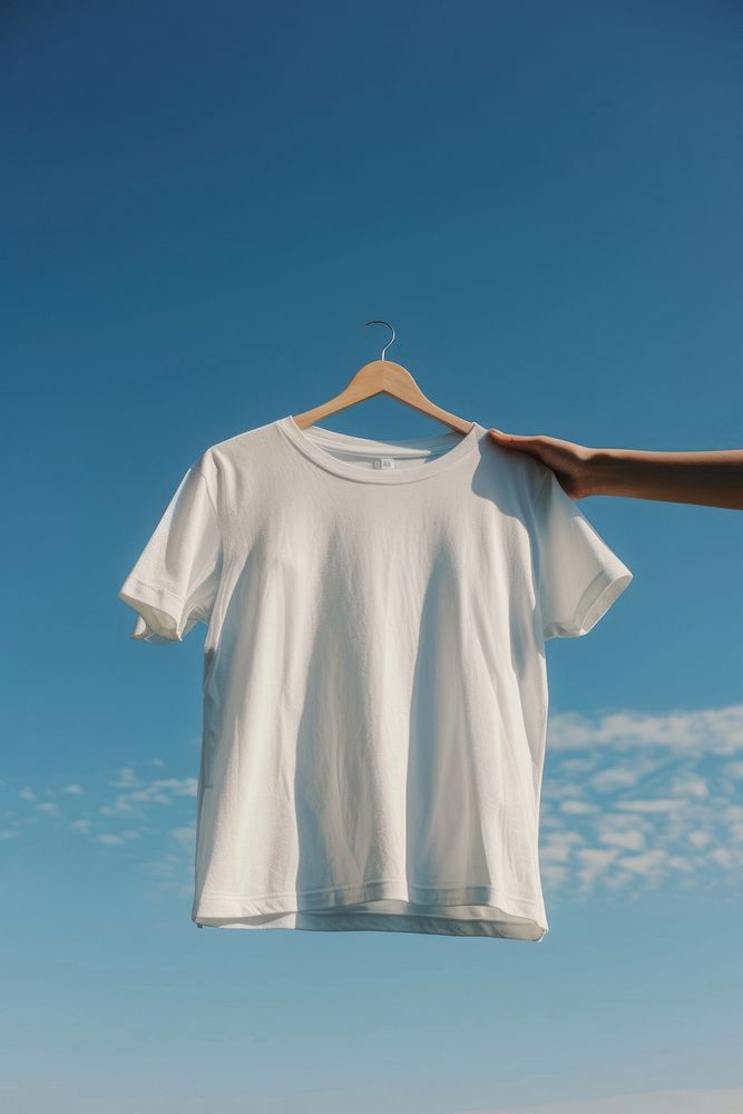 Hand holding hanger with white t shirt outdoors t-shirt sleeve.