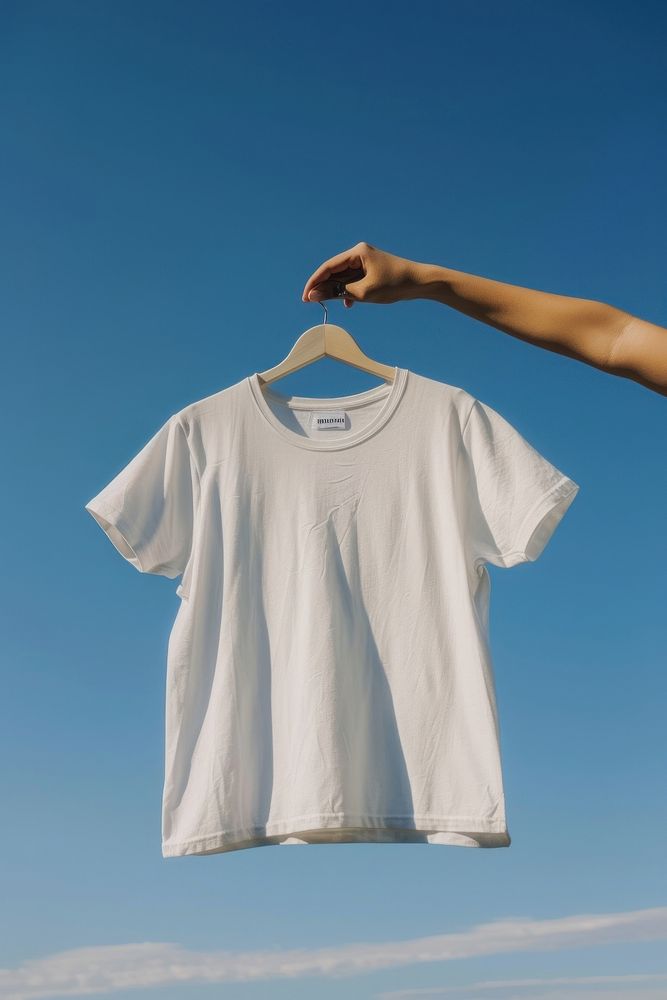 Hand holding hanger with white t shirt outdoors t-shirt sleeve.