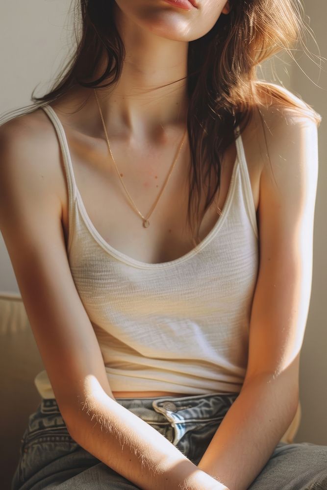 Detail of woman gentle skin in color pastel color tank top necklace jewelry sitting.