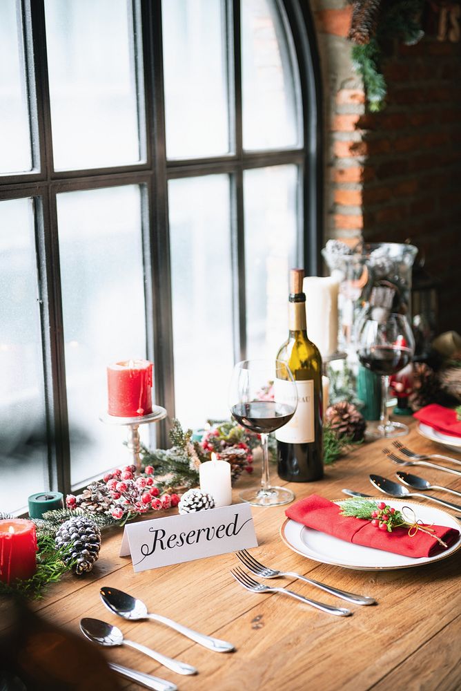 Festive table setting with wine, candles, and holiday decor. Reserved sign, wine glasses, and red accents create a cozy…