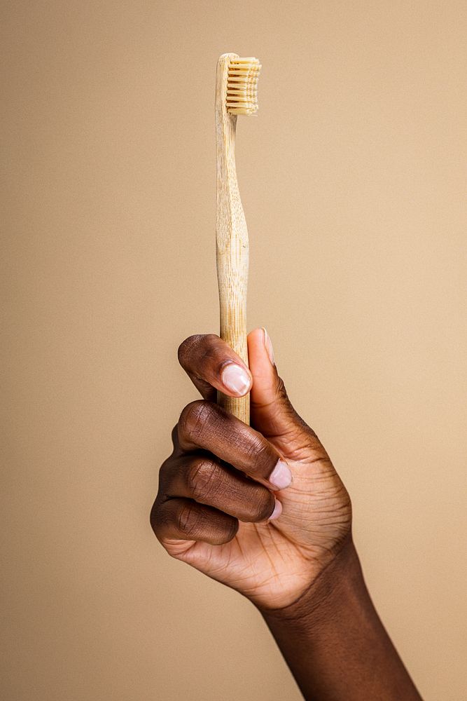 Hand holding a bamboo toothbrush against a beige background. Eco-friendly bamboo toothbrush in a hand. Sustainable bamboo…