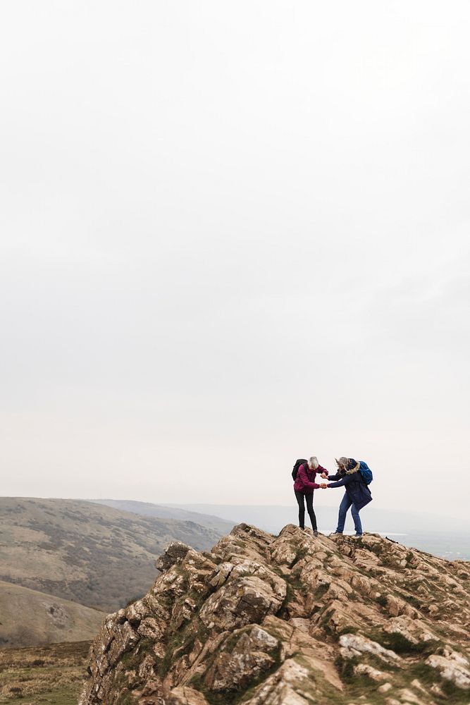 Three people hiking on a rocky mountain peak under a cloudy sky. Outdoor adventure, hiking, and nature exploration on a…