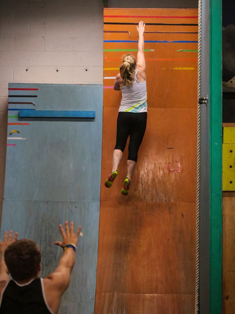 Kim Wienches reaches for the top of the Curved Wall at Pinnacle Parkour Academy. Original public domain image from Flickr