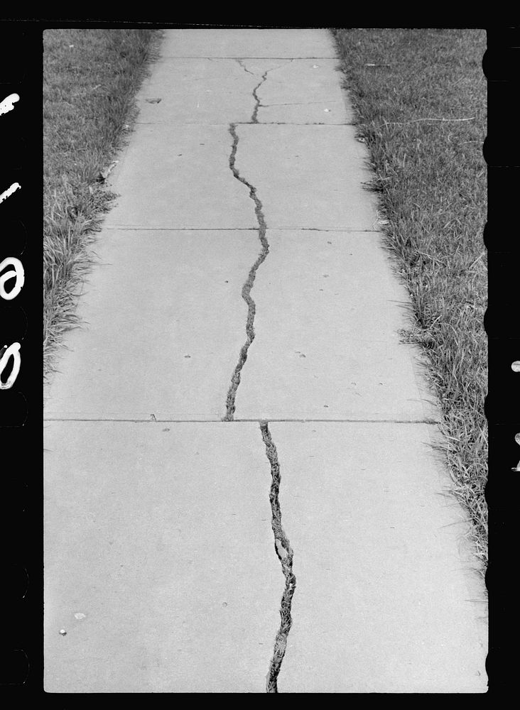 Grass growing in cracks of sidewalk, Grundy Center, Iowa. Sourced from the Library of Congress.