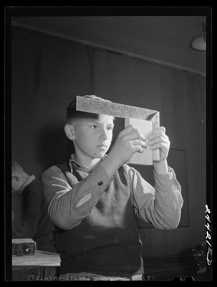 Boy using right angle square in woodworking shop at the homestead school. Dailey, West Virginia. Sourced from the Library of…