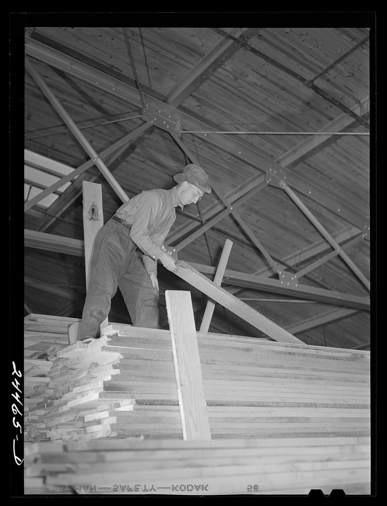 Worker unloading lumber from stacks. Dimension lumber plant. Dailey, West Virginia. Sourced from the Library of Congress.