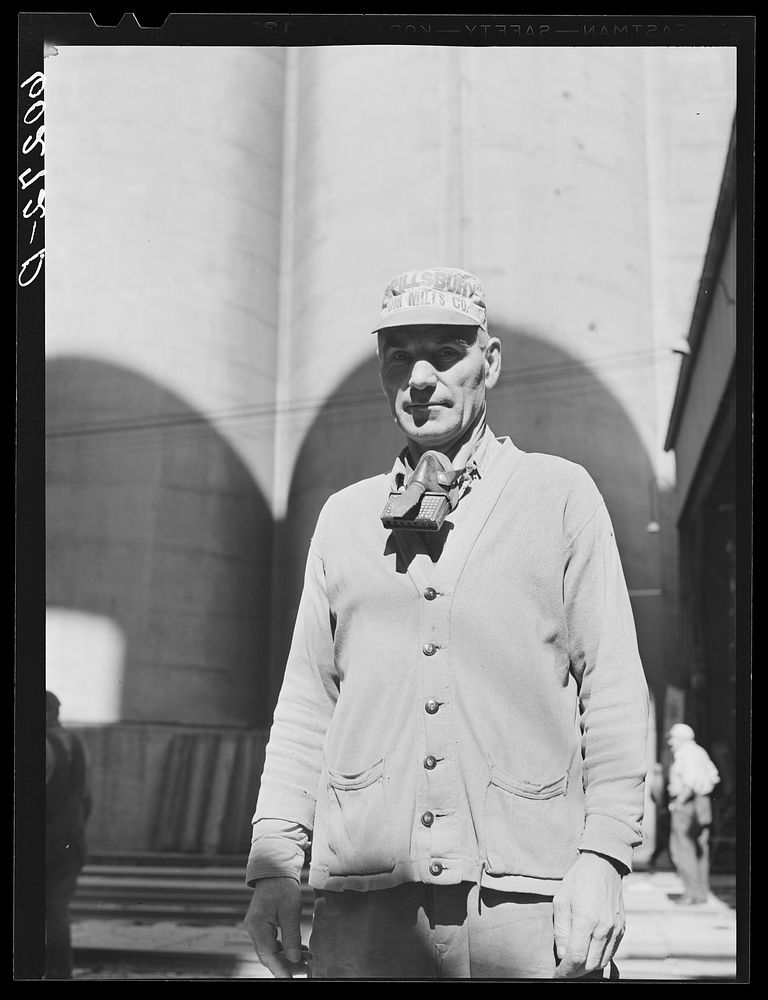Grain elevator employee. Minneapolis, Minnesota. He wears mask while unloading grain from freight cars. Sourced from the…