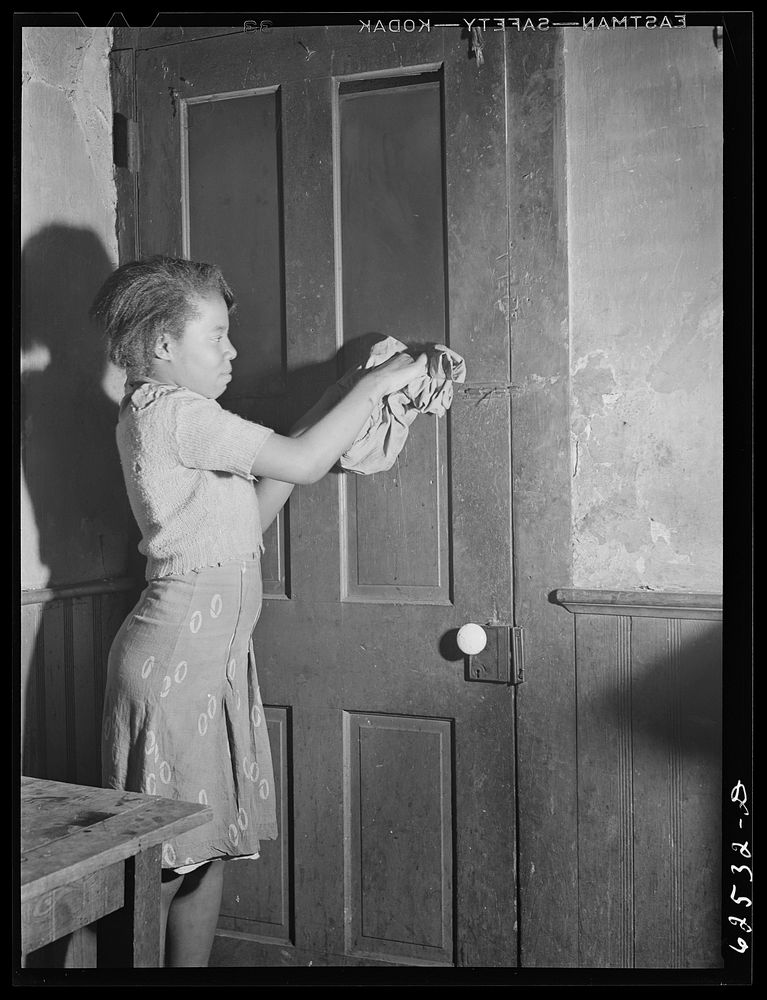 Girl stuffing rag in hole in door to keep cold out.   district. Norfolk, Virginia. Sourced from the Library of Congress.