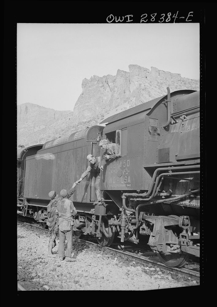 An American crew in the cab of an American engine are at a stop on the railway passing the time with some Iranian boys…