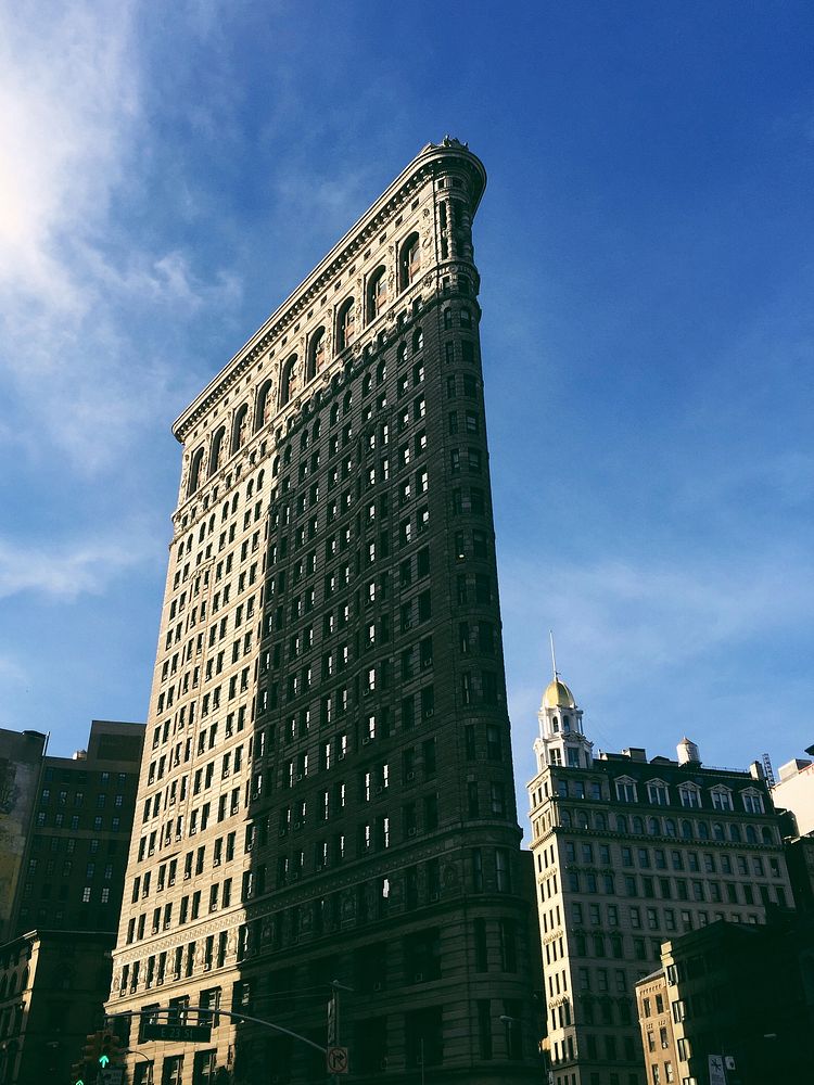 Flatiron building in New York with cloudy blue sky and building shadow on windows. Original public domain image from…
