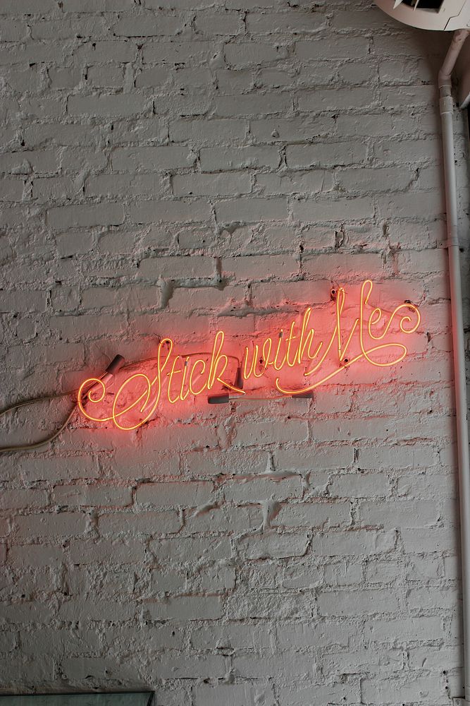 A red neon with “stick with me” written in cursive on a white brick wall. Original public domain image from Wikimedia Commons