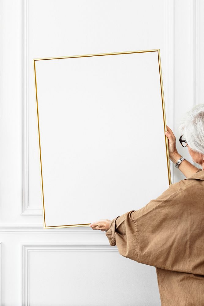 Senior woman hanging a blank picture frame on a white wall