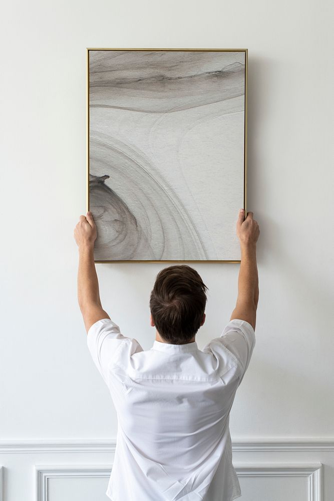Abstract painting being hung by a young man on a white minimal wall