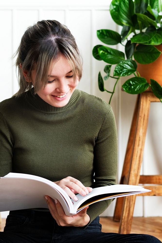 Young woman reading a book about gardening surrounded by potted plants