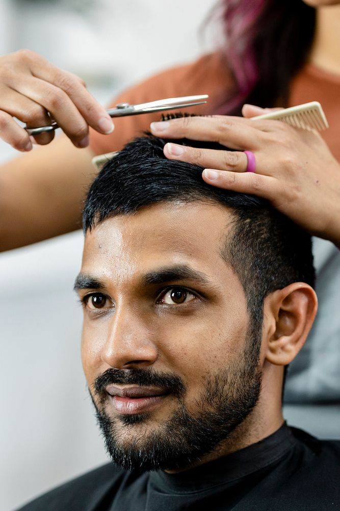 Man getting a haircut from a hair stylist at a barber shop 