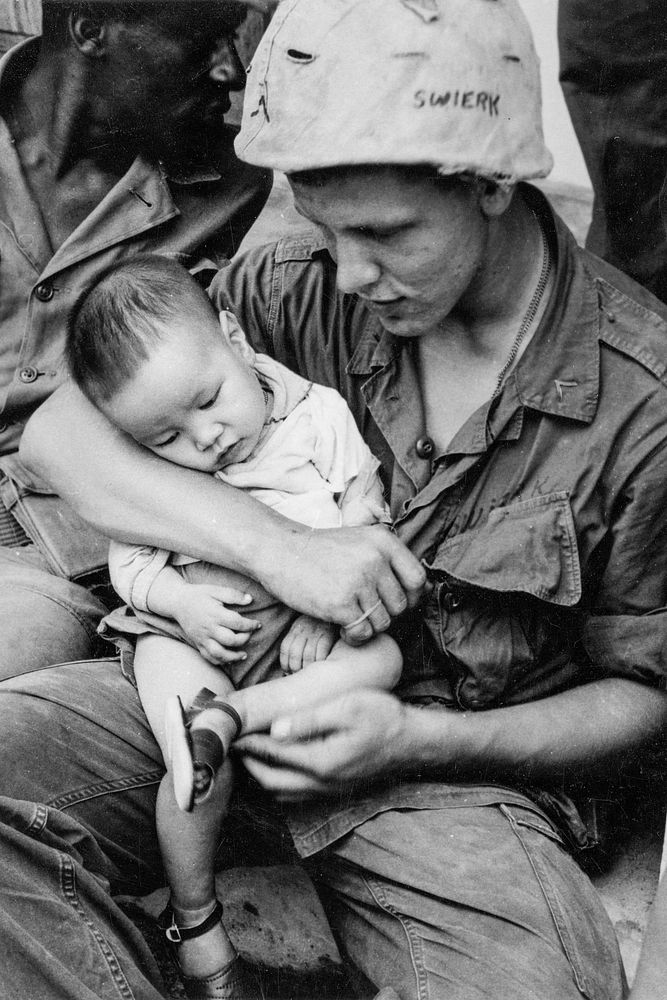  A soldier, whose helmet says "Swierk," holds a Vietnamese child during Vietnam War.