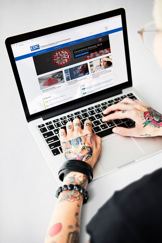 Tattooed man reading coronavirus updates from a laptop mockup with editorial graphic from https://www.cdc.gov accessed on…