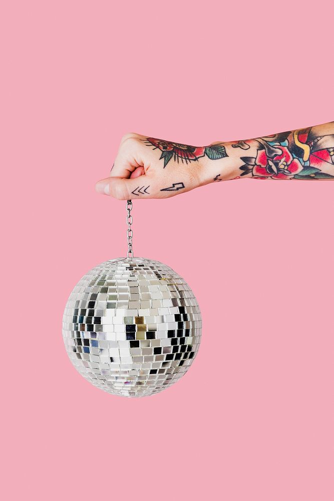 Tattooed hand holding Christmas glass ball with light pink background