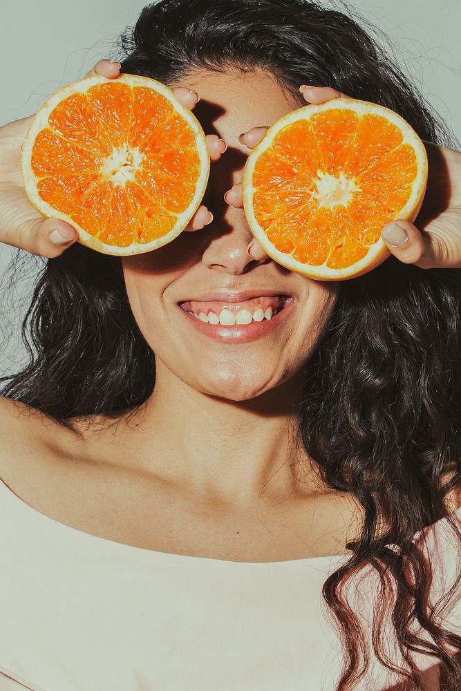 Cheerful woman with sliced oranges covering her eyes 