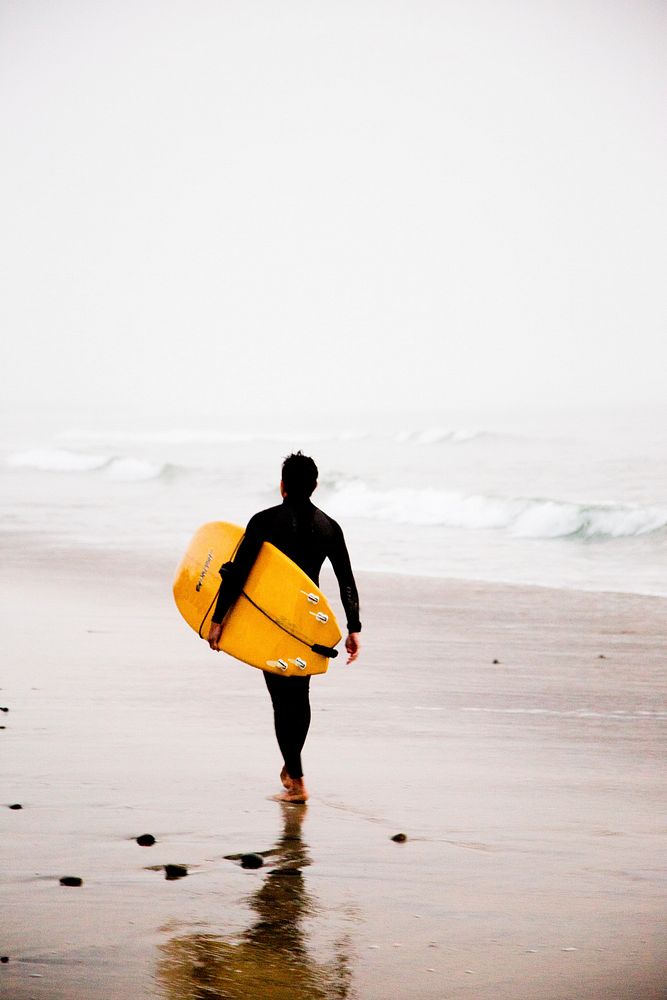 Surfer with the surfboard walking down the wet sand beach at Carlsbad. Original public domain image from Wikimedia Commons