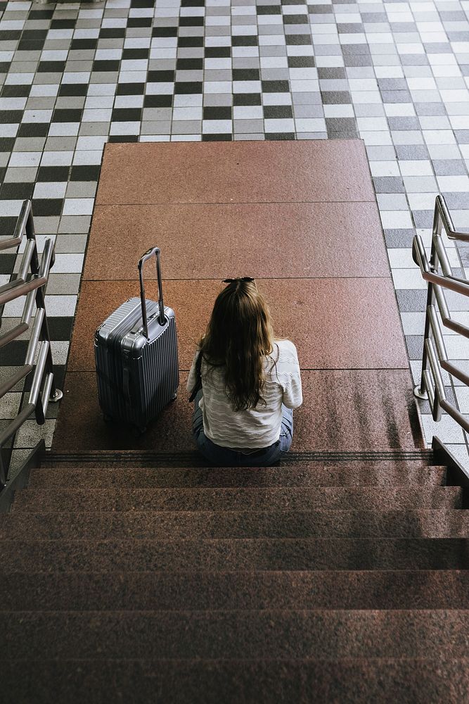 Woman with a suitcase sitting on the stairs waiting for the train during the coronavirus outbreak 