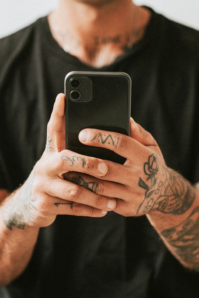 Alternative tattooed man in black tee using smartphone