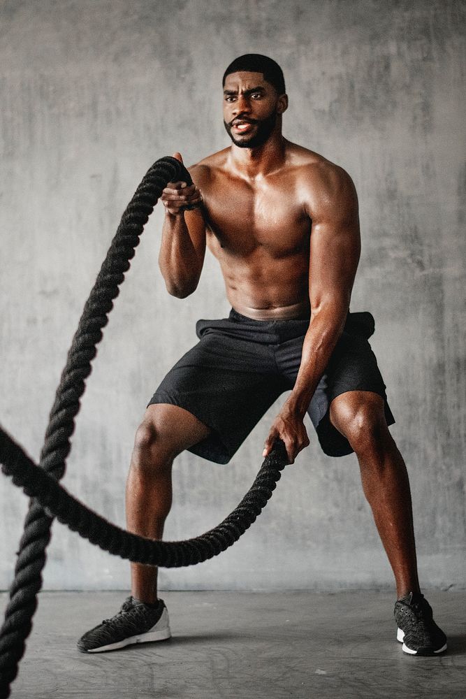 Muscular man working out on the battle ropes in a gym