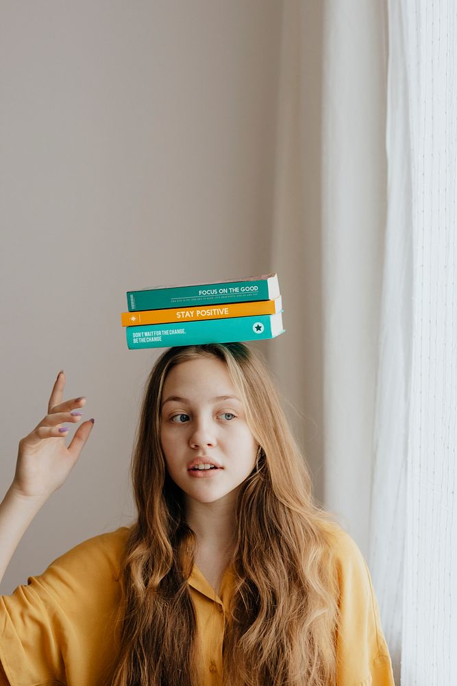 Cheerful blond girl balancing books on her head