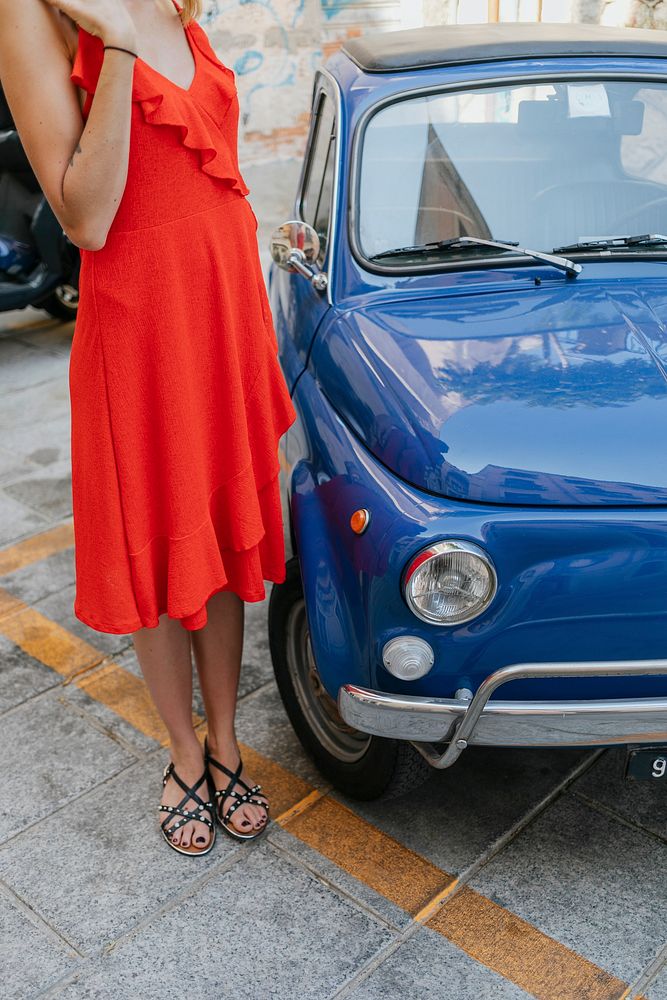Woman in a red dress standing by a blue car