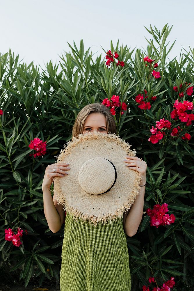Woman holding a straw hat in front of a shrub