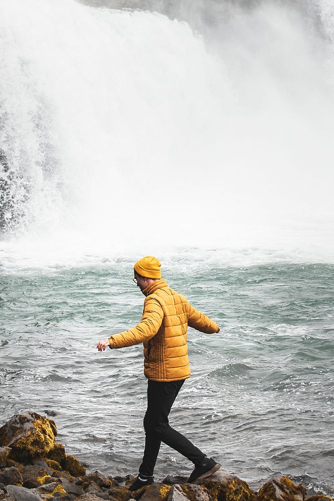Man by the waterfall walking on rocks 