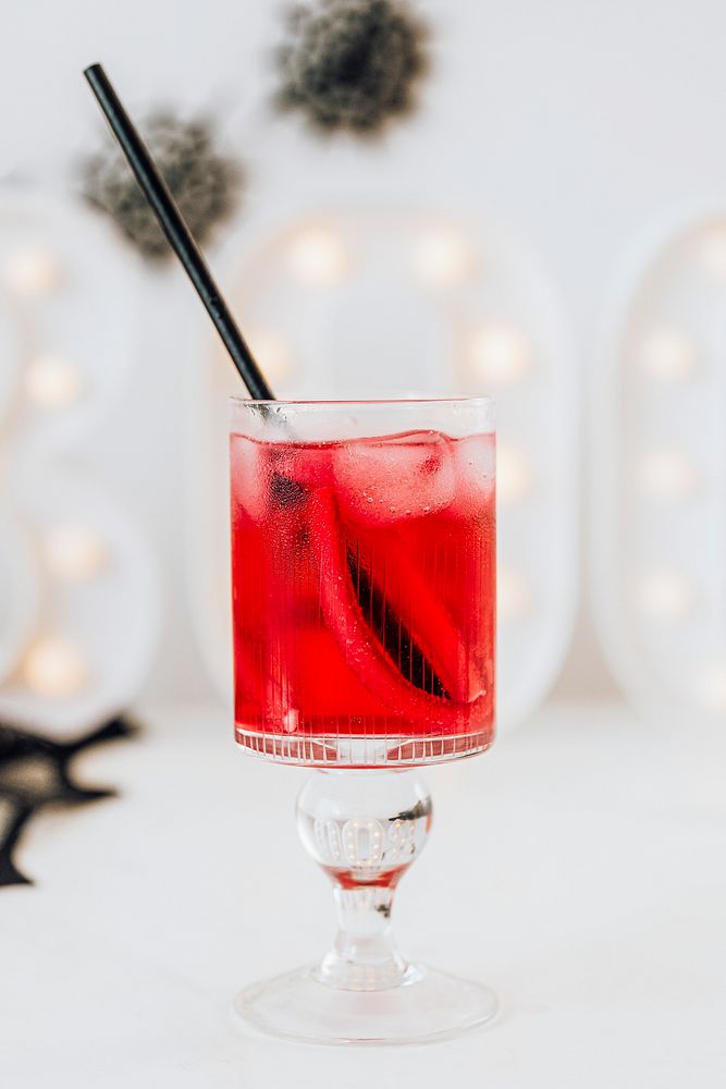 Red drink in a glass with a straw on a white table 