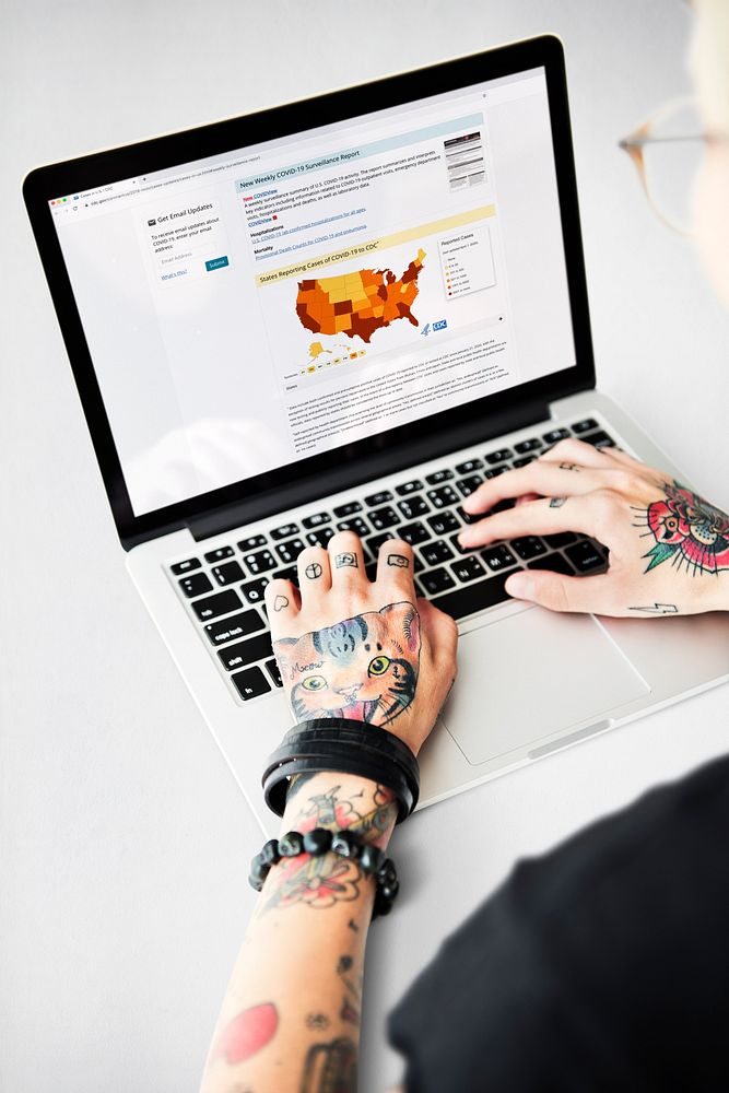 Tattooed man reading coronavirus updates from a laptop mockup with editorial graphic from…