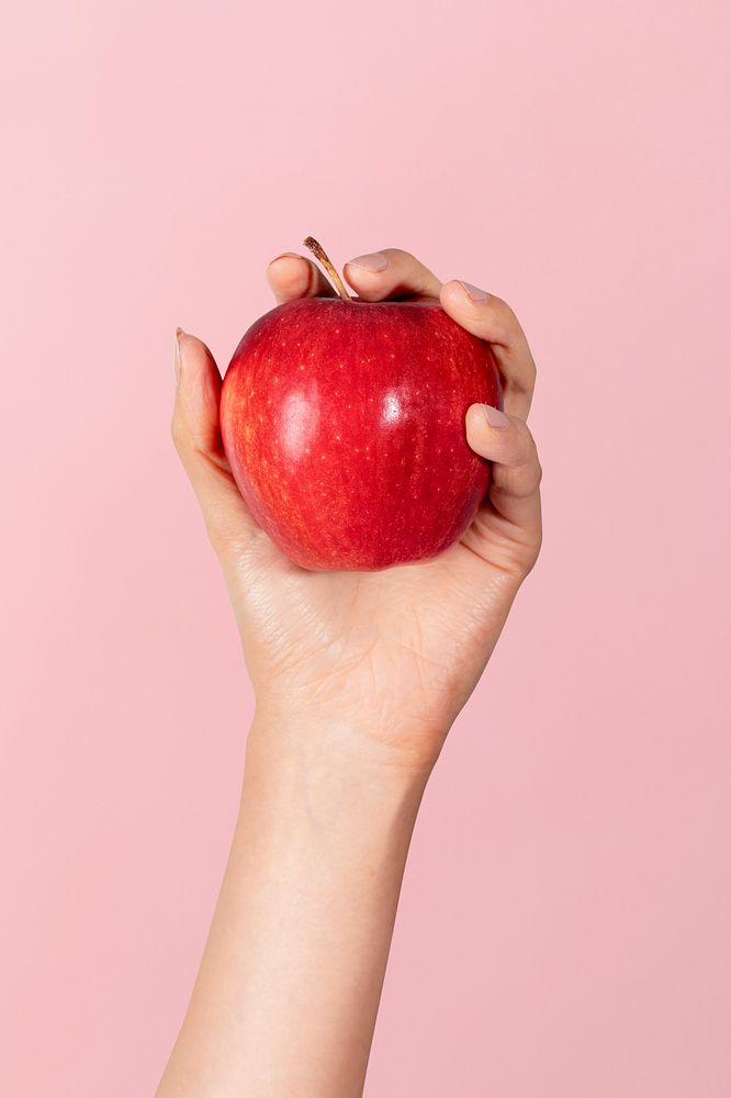 Woman holding a ripe apple against a pink background