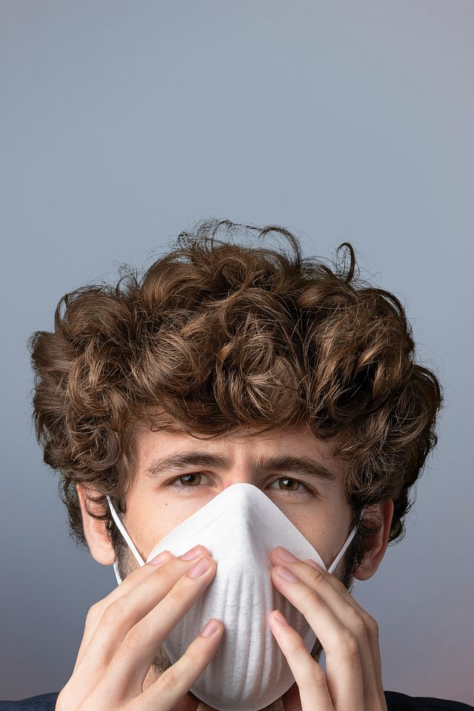 Young Caucasian man wearing a disposable protection mask in a gray background