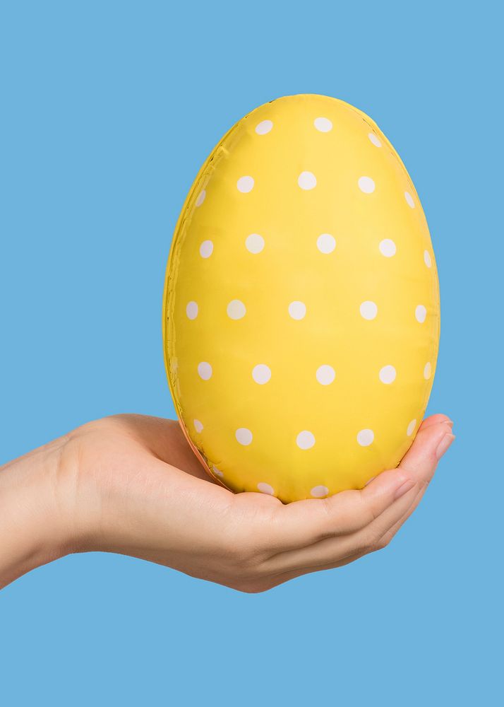 Hand holding a white polka dot patterned yellow egg on a blue background