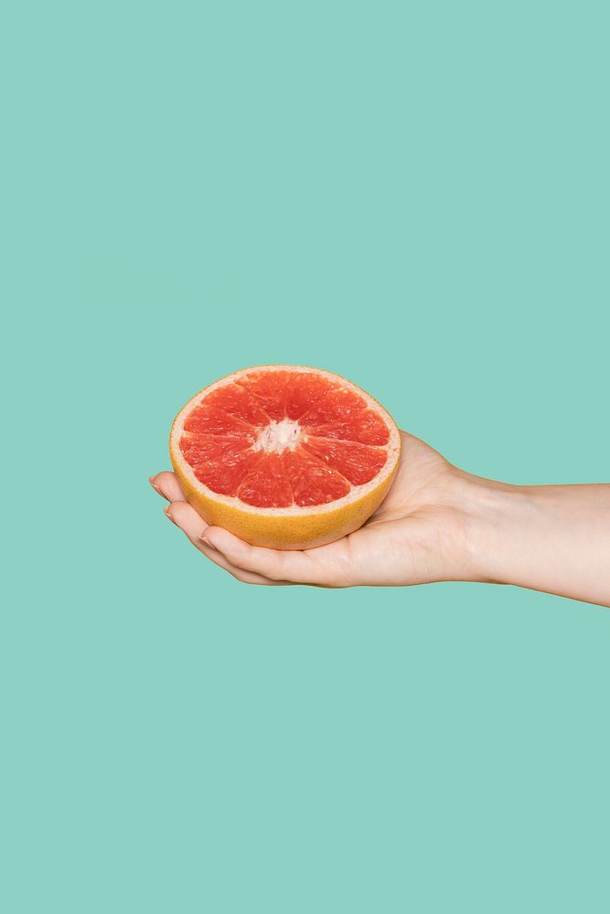 Hand holding grapefruit, green background