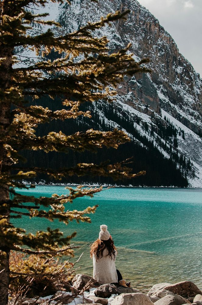 A woman in a knit cap sitting on rocks on the shore of Lake Louise. Original public domain image from Wikimedia Commons