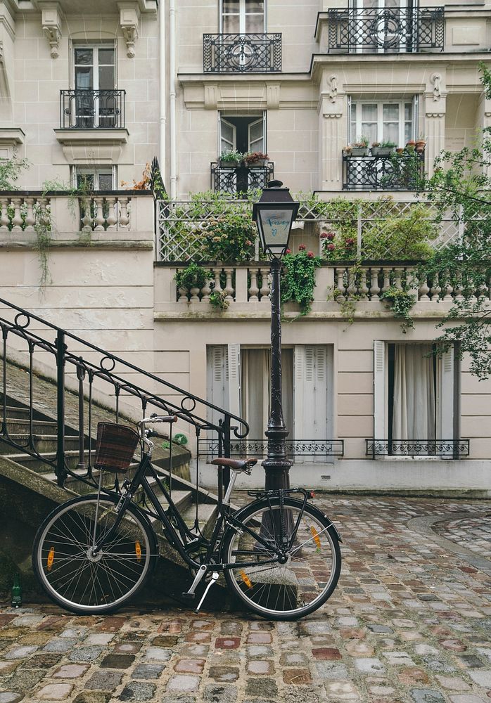 A bicycle resting against a flight of stairs and a lamppost with French buildings in the background.. Original public domain…