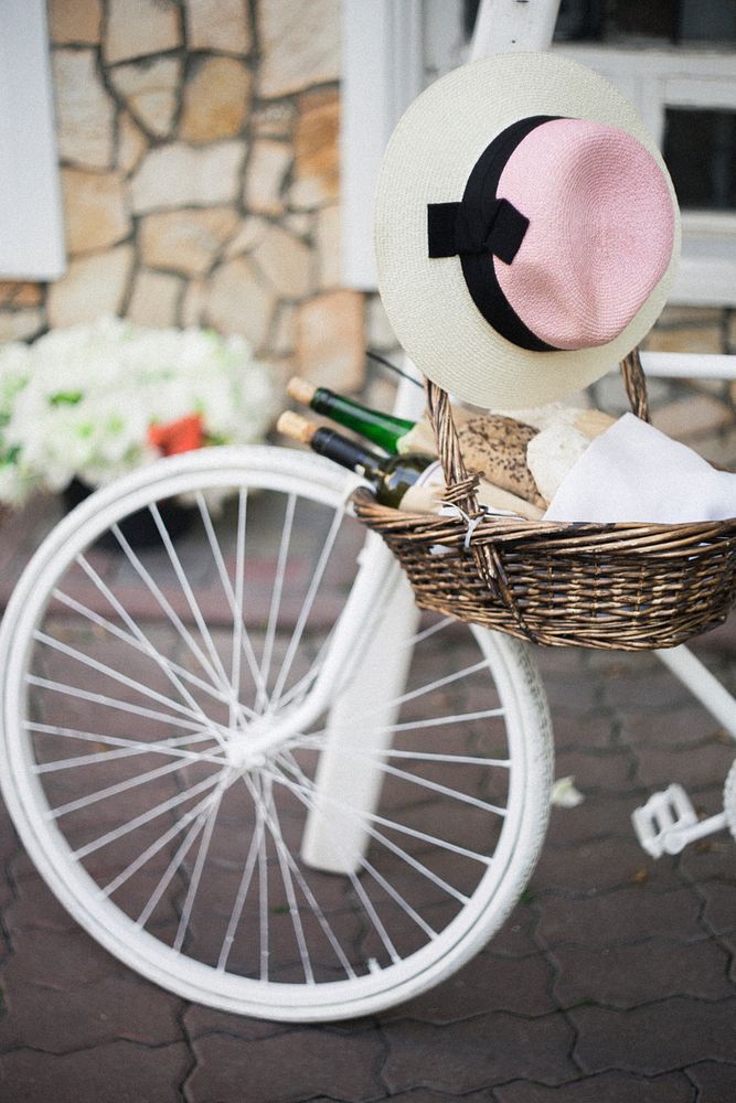A basket with two bottles of wine and fresh bread hanging from the handlebar of a white bicycle. Original public domain…