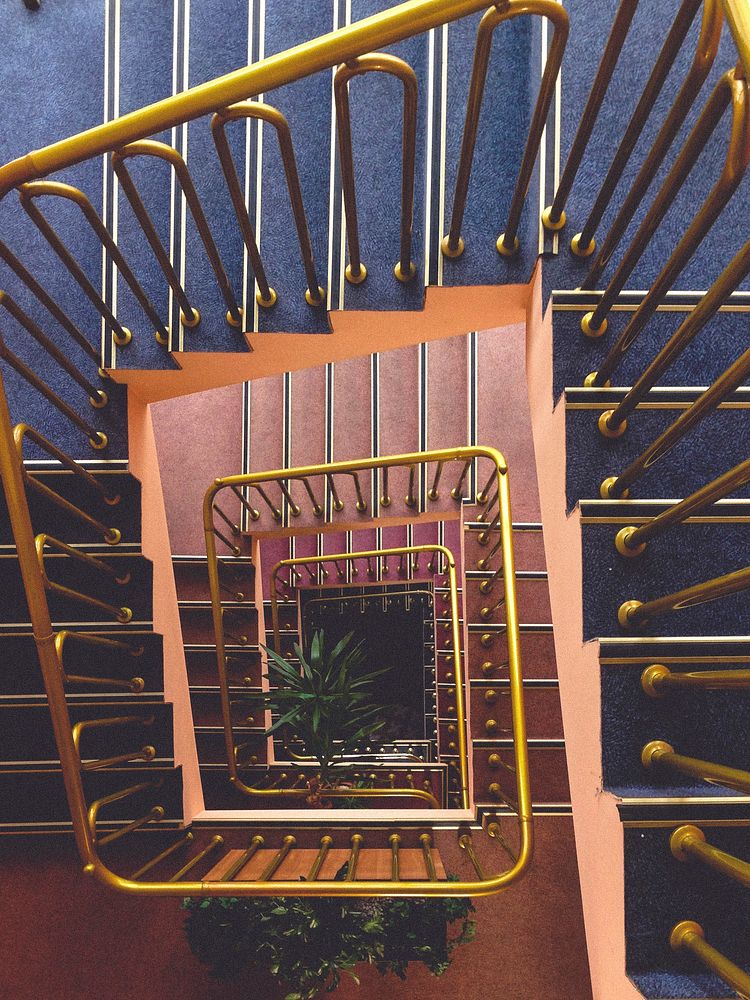 Looking down at a vintage spiral staircase with a gold banister. Original public domain image from Wikimedia Commons