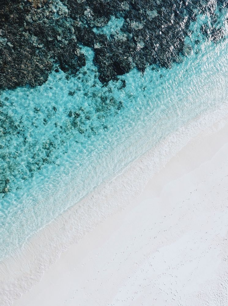 Drone view of a white sandy beach by the clear ocean in Bathalaa. Original public domain image from Wikimedia Commons