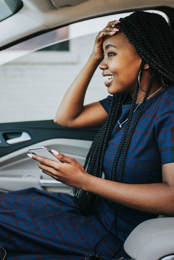 Happy black woman holding her head with a phone in the car
