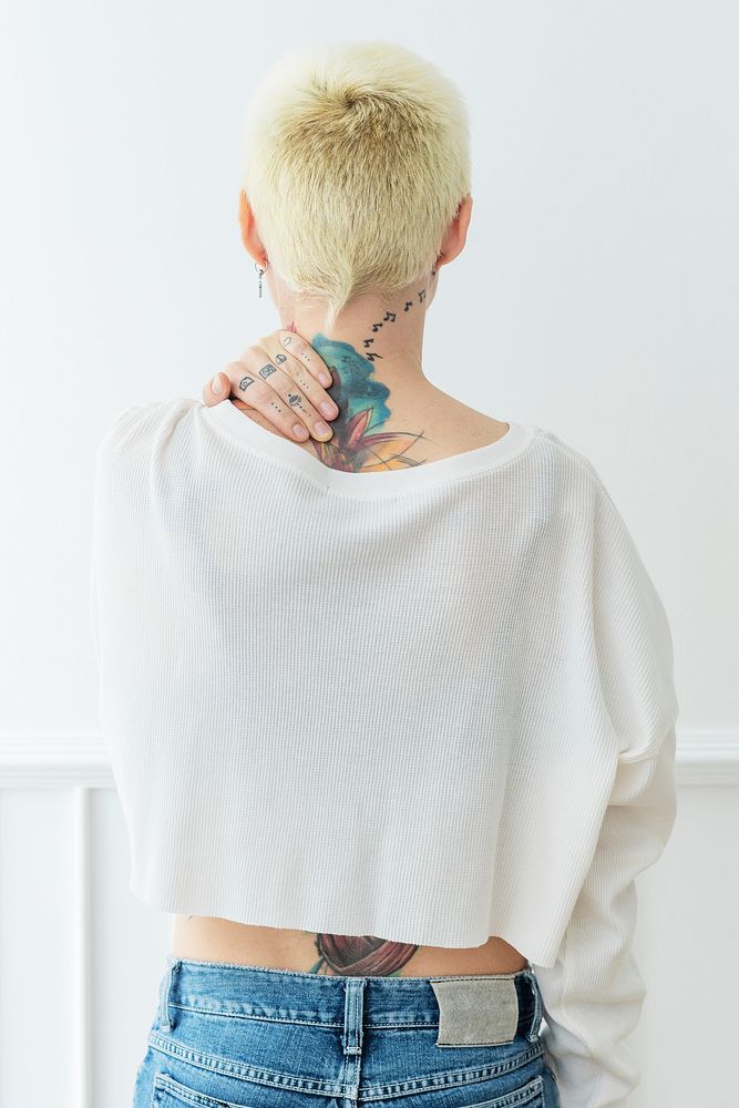 Tattooed woman in a white shirt touching her neck