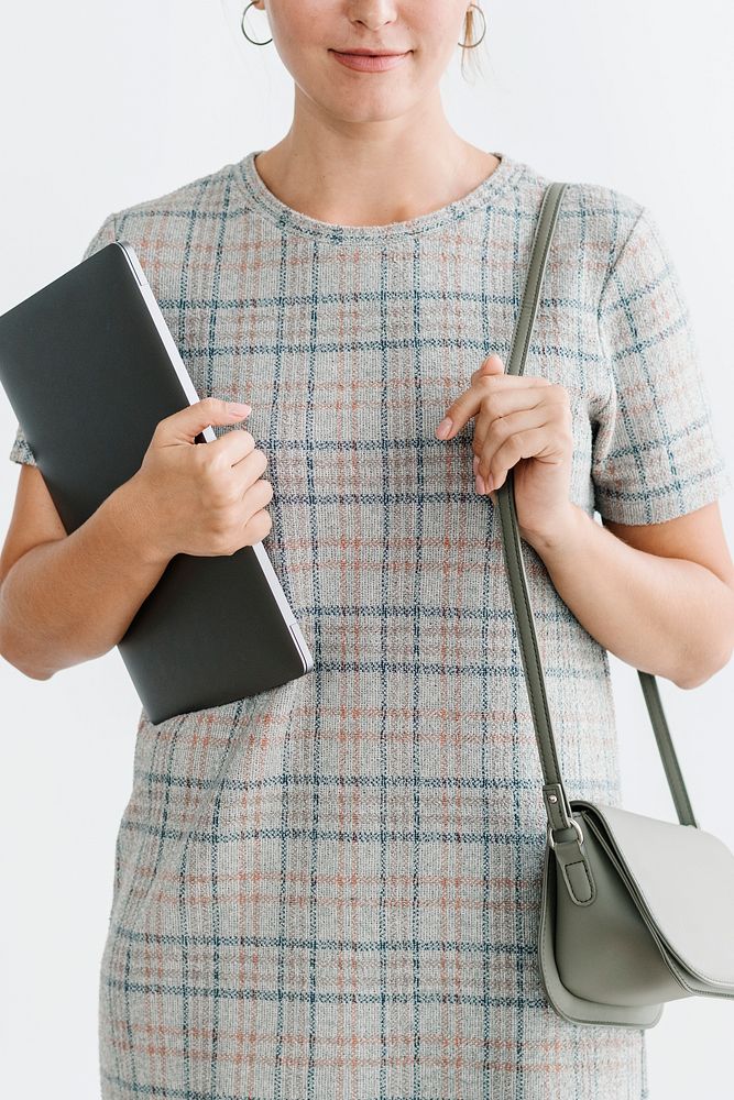 Woman in a gray plaid dress holding a laptop