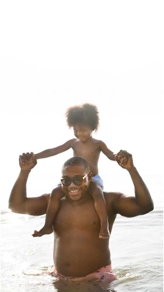 African American dad and son playing piggyback in the sea text space
